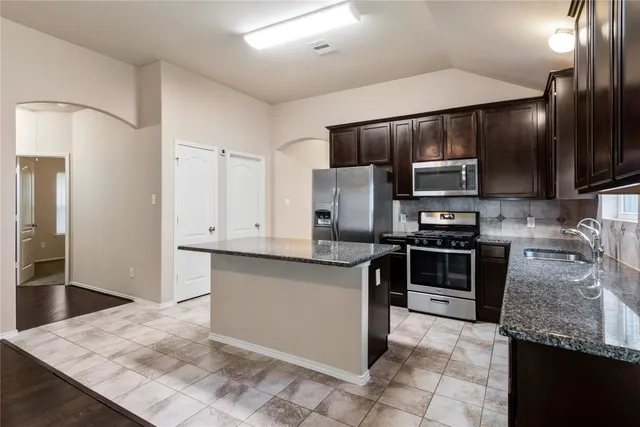 a kitchen with stainless steel appliances granite countertop a refrigerator a stove and a sink with wooden cabinets