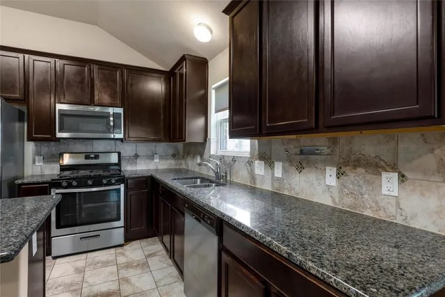 a kitchen with granite countertop stainless steel appliances a stove sink and cabinets