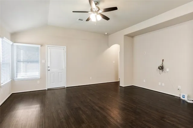 an empty room with wooden floor chandelier fan and windows