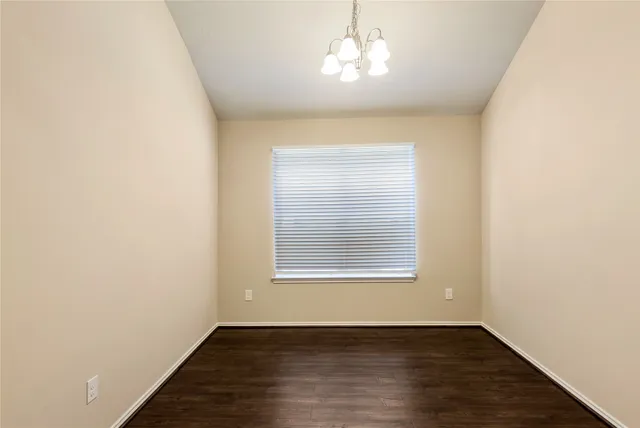 an empty room with wooden floor chandelier and window