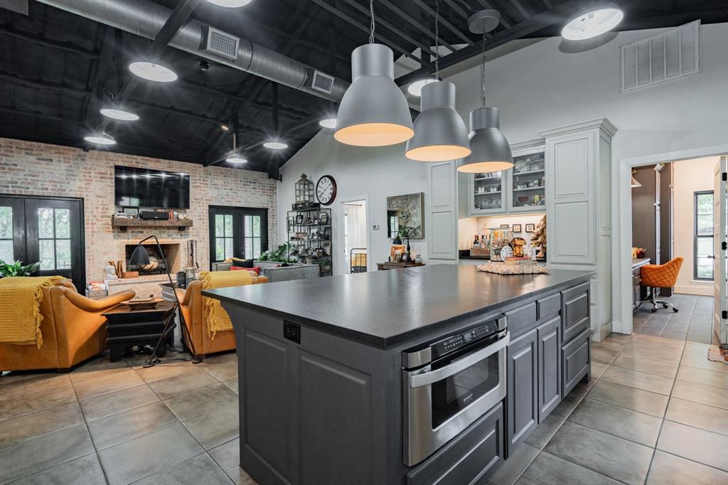 853 County Road 2215 Decatur, TX 76234 - Photo 39 of 39 Kitchen with brick wall, dark countertops, glass insert cabinets, open floor plan, and a kitchen island