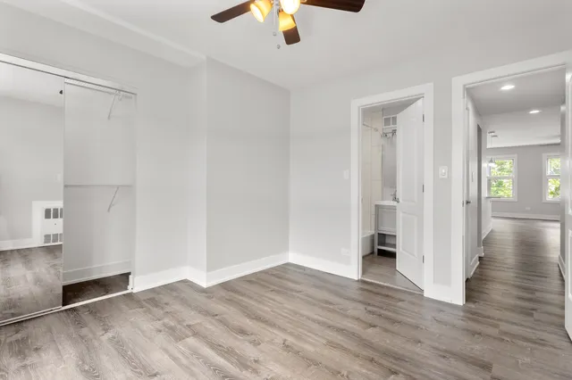 a view of an empty room with wooden floor and a ceiling fan