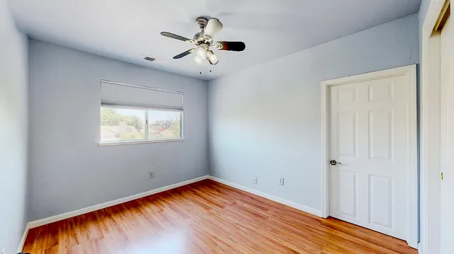 a view of an empty room with wooden floor and a fan