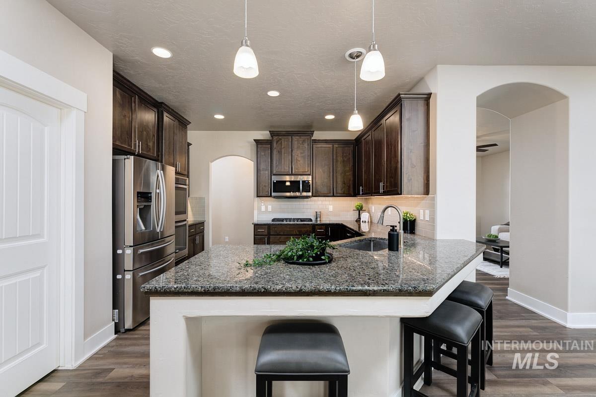 3902 North Rotaldo Avenue Meridian, ID 83646 - Photo 12 of 34 Kitchen with arched walkways, dark brown cabinetry, stainless steel appliances, tasteful backsplash, and decorative light fixtures