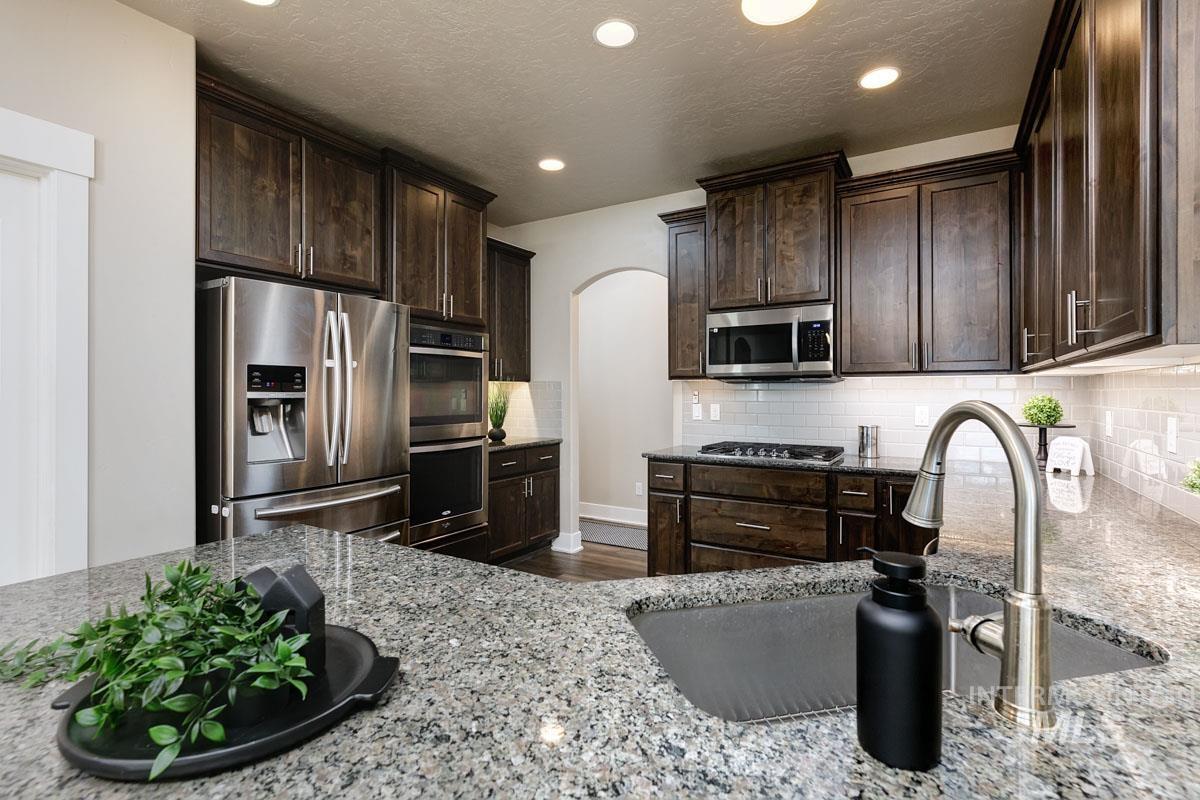 3902 North Rotaldo Avenue Meridian, ID 83646 - Photo 13 of 34 Kitchen featuring arched walkways, dark brown cabinets, appliances with stainless steel finishes, light stone counters, and recessed lighting