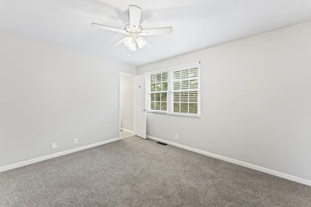 an empty room with a chandelier fan and windows