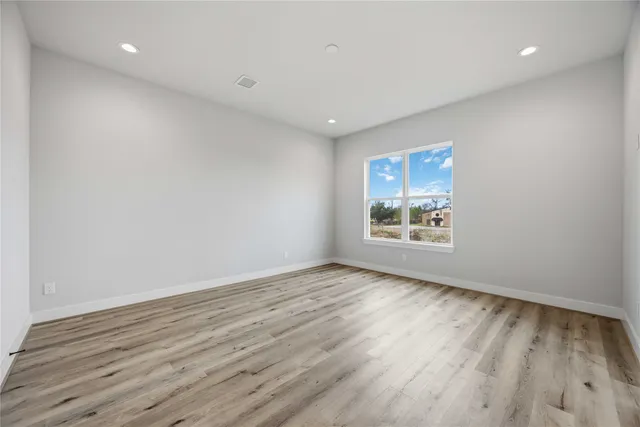 a view of an empty room with wooden floor closet and windows