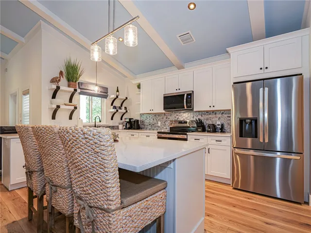 a kitchen with stainless steel appliances kitchen island granite countertop a refrigerator a stove top oven a sink dishwasher and white cabinets with wooden floor