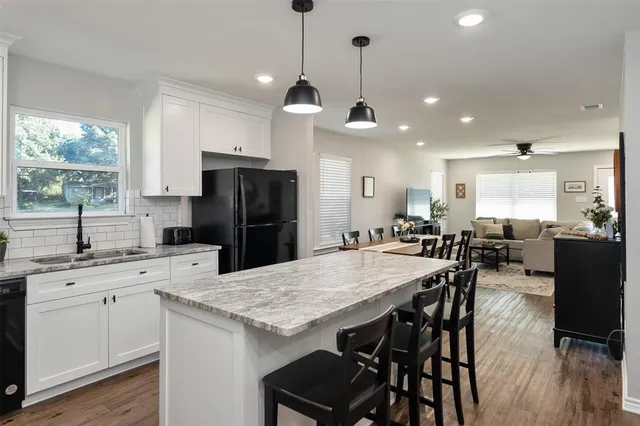 a kitchen with stainless steel appliances kitchen island granite countertop a refrigerator a stove a sink a dining table and chairs with wooden floor