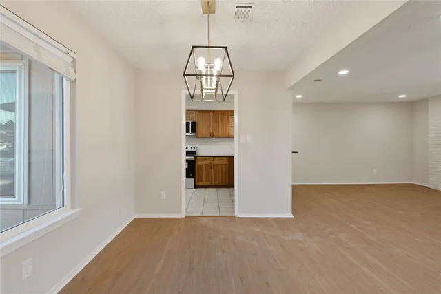 a view of empty room with wooden floor and kitchen view