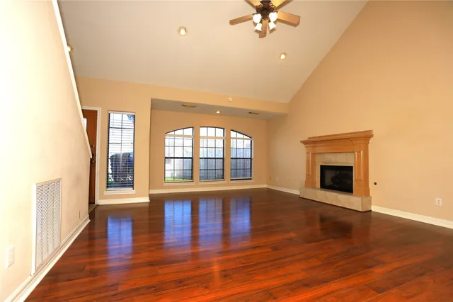 an empty room with wooden floor fan and windows