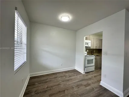 a view of a kitchen and an empty room with wooden floor and a window