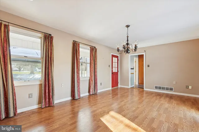 an empty room with wooden floor chandelier and windows