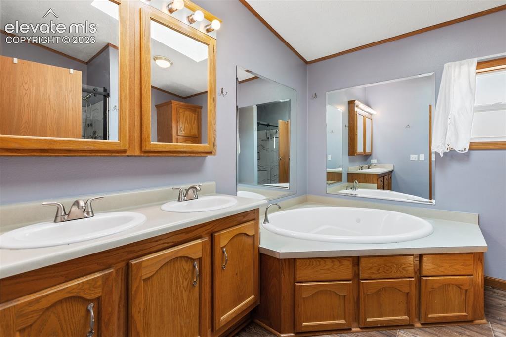 1350 South Calhan Highway Yoder, CO 80864 - Photo 31 of 45 Spacious bathroom featuring a built-in corner soaking tub, a dual vanity with light-toned countertops, and wood-finish cabinetry