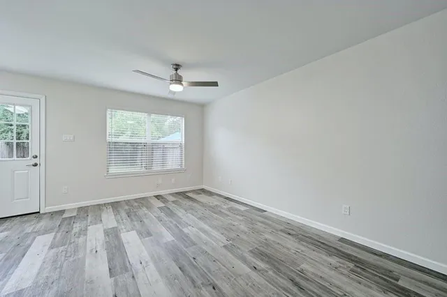 an empty room with wooden floor chandelier fan and windows