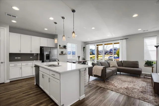 a open kitchen with stainless steel appliances granite countertop a stove top oven a sink dishwasher a dining table and chairs with wooden floor