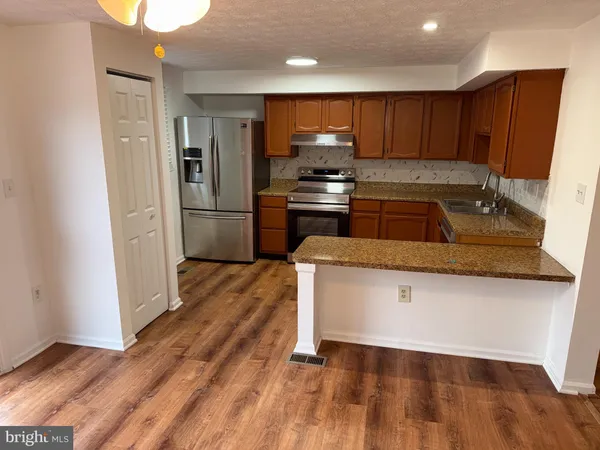 a kitchen with granite countertop wooden floors stainless steel appliances a sink and a counter