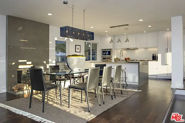 a kitchen with stainless steel appliances kitchen island granite countertop a dining table chairs and a refrigerator