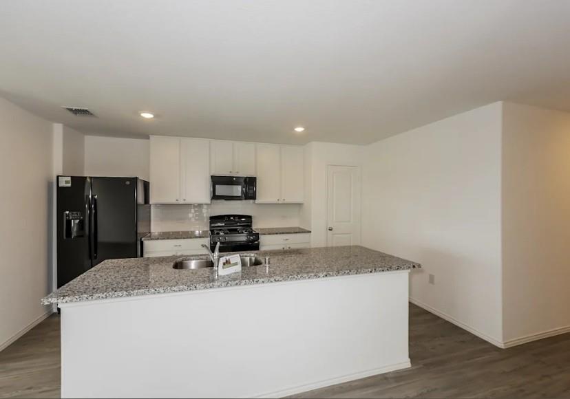 10225 Hackberry Spg Way Crowley, TX 76036 - Photo 5 of 11 Kitchen featuring light stone counters, white cabinets, a center island with sink, black appliances, and dark wood finished floors