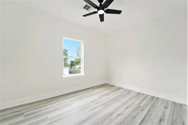 an empty room with wooden floor ceiling fan and windows