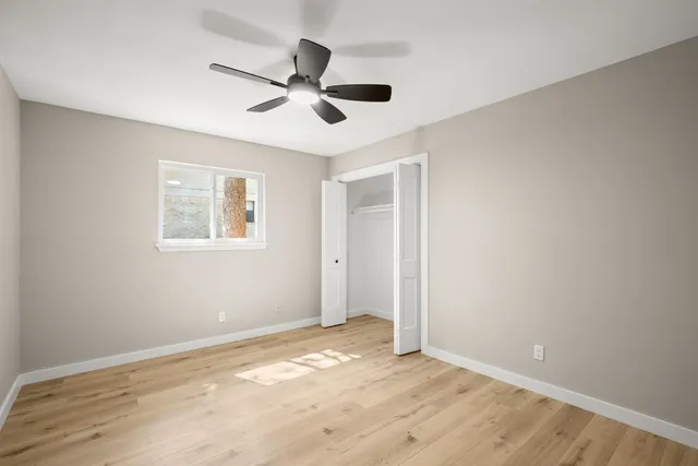 a view of an empty room with wooden floor and a ceiling fan