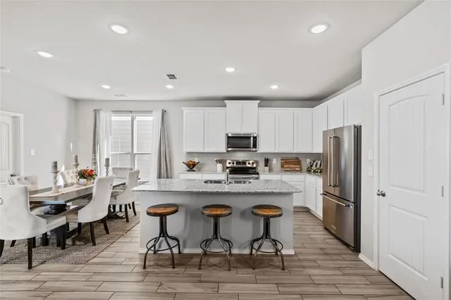 a large white dining hall with stainless steel appliances granite countertop a dining table and chairs