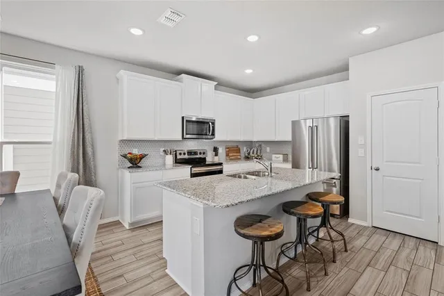 a kitchen with stainless steel appliances a microwave a stove a refrigerator a sink a dining table and chairs