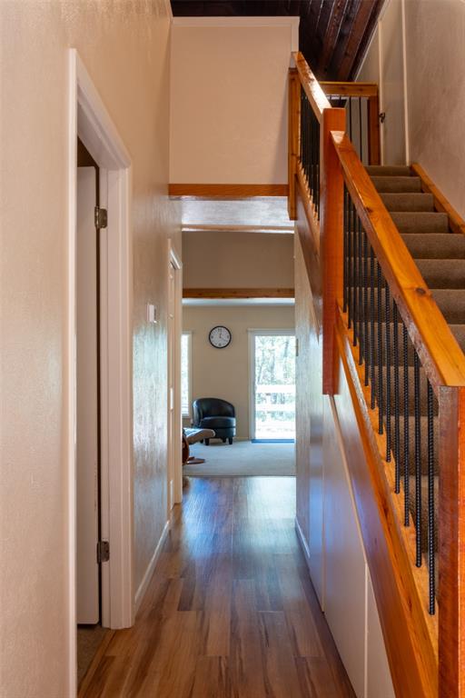 167 Blue Water Point Holly Lake Ranch, TX 75765 - Photo 10 of 27 Wood-finish flooring, staircase with natural wood handrail and black metal balusters, exposed wood beam ceiling, and neutral wall tones