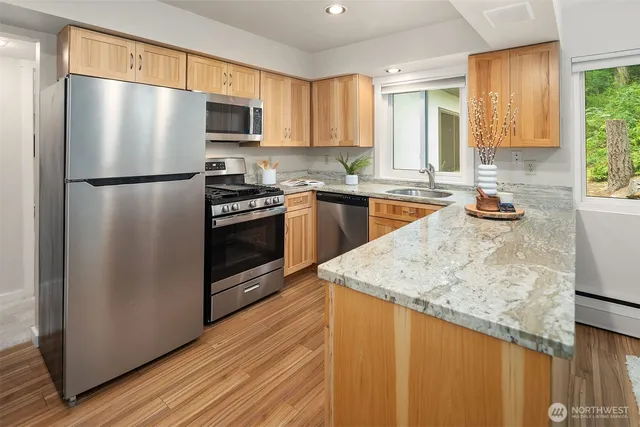 a kitchen with stainless steel appliances granite countertop a refrigerator a stove top oven a sink and dishwasher with wooden floor