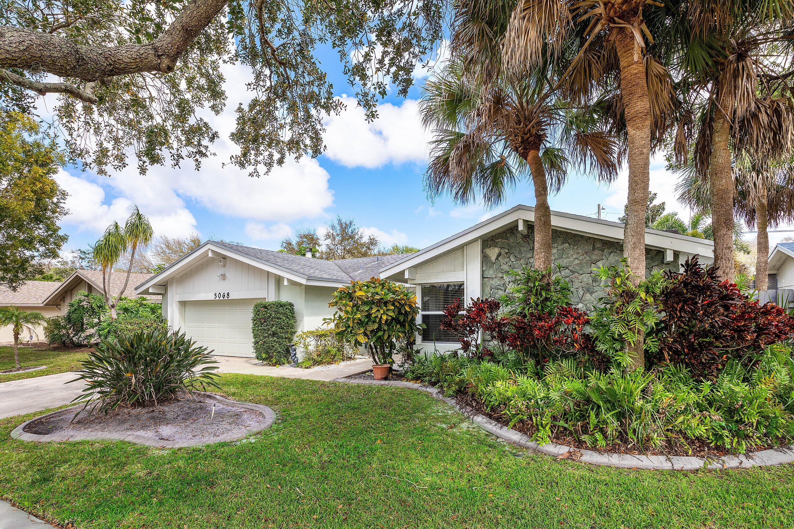 3068 Northwest 25th Way Boca Raton, FL 33434 - Photo 3 of 43 a front view of a house with a garden and trees