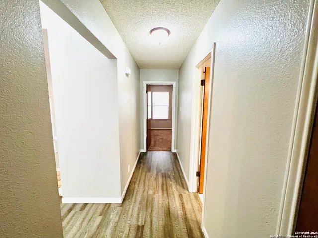 a view of a hallway with wooden floor and a bathroom
