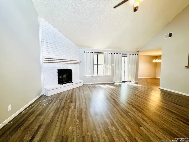 a view of an empty room with wooden floor fireplace and a window