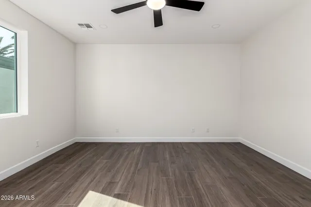 a view of an empty room with wooden floor a ceiling fan and window