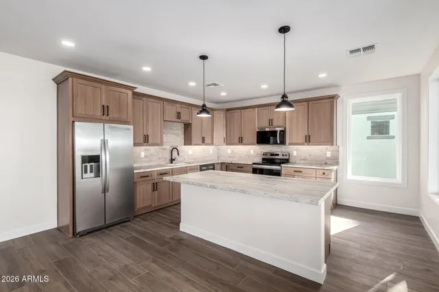 a kitchen with stainless steel appliances kitchen island granite countertop a stove a sink a refrigerator and white cabinets with wooden floor