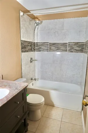 a bathroom with a granite countertop bathtub shower sink vanity and toilet