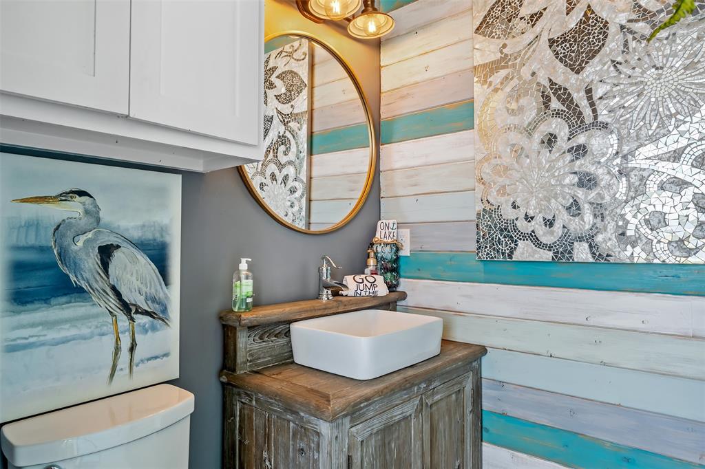 16241 Big Oak Bay Road Tyler, TX 75707 - Photo 30 of 40 Distressed wood vanity with a white vessel sink, gold-framed round mirror, and a wall-mounted light fixture