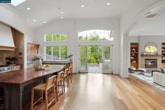 a dining hall with stainless steel appliances granite countertop a stove a sink a refrigerator white cabinets and couches with wooden floor