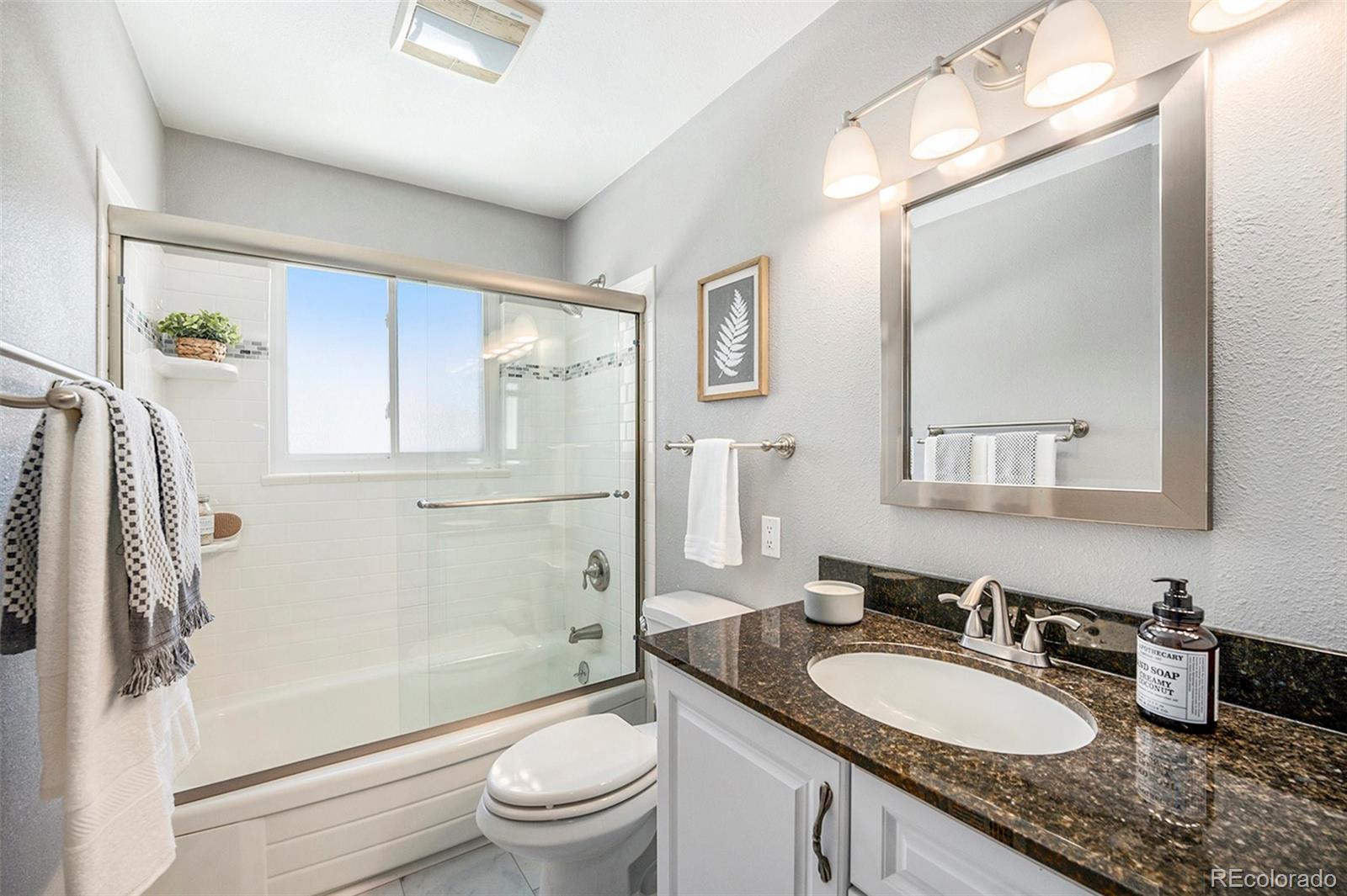 3582 Wright Street Wheat Ridge, CO 80033 - Photo 19 of 31 a bathroom with a granite countertop sink a toilet a mirror and shower