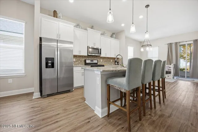 a kitchen with stainless steel appliances granite countertop a refrigerator a stove a sink dishwasher a dining table and chairs with wooden floor