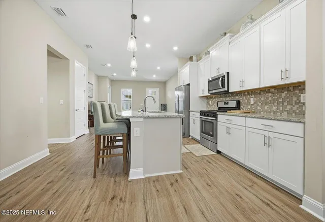 a kitchen with stainless steel appliances granite countertop a refrigerator a stove top oven a sink dishwasher and white cabinets with wooden floor