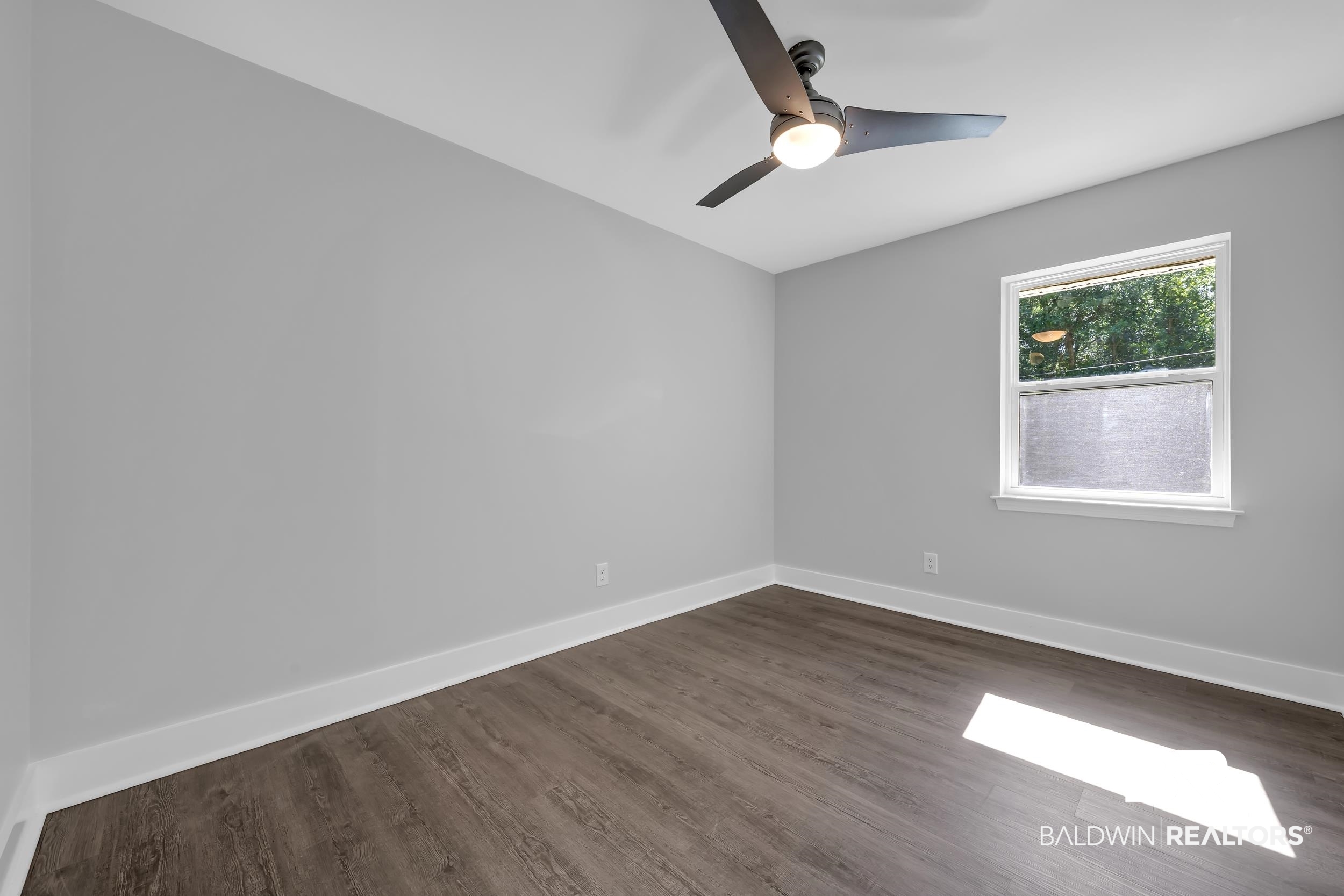 2712 Shelton Beach Rd Extension Mobile, AL 36613 - Photo 12 of 24 Light gray walls complement the wood-finish flooring in this room featuring a ceiling fan with integrated lighting and a white-framed window