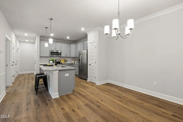 a kitchen with kitchen island granite countertop stainless steel appliances a refrigerator oven a sink dishwasher and white cabinets with wooden floor