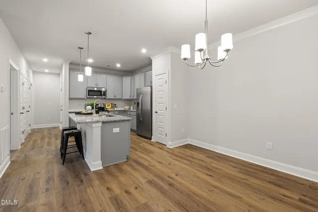 a kitchen with kitchen island granite countertop stainless steel appliances a refrigerator oven a sink dishwasher and white cabinets with wooden floor