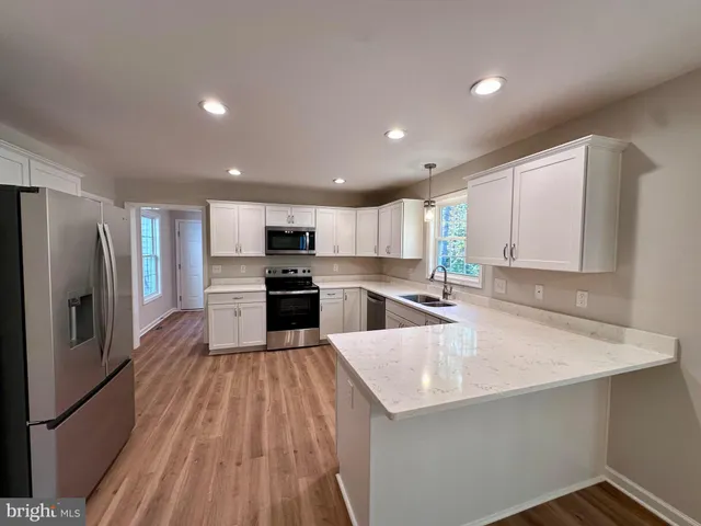 a large kitchen with stainless steel appliances kitchen island granite countertop a refrigerator a sink dishwasher a stove and white countertops with wooden floor