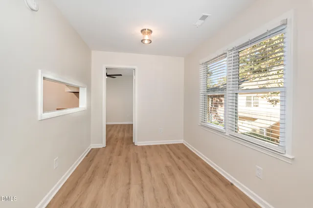 an empty room to hallway with wooden floor and a ceiling fan