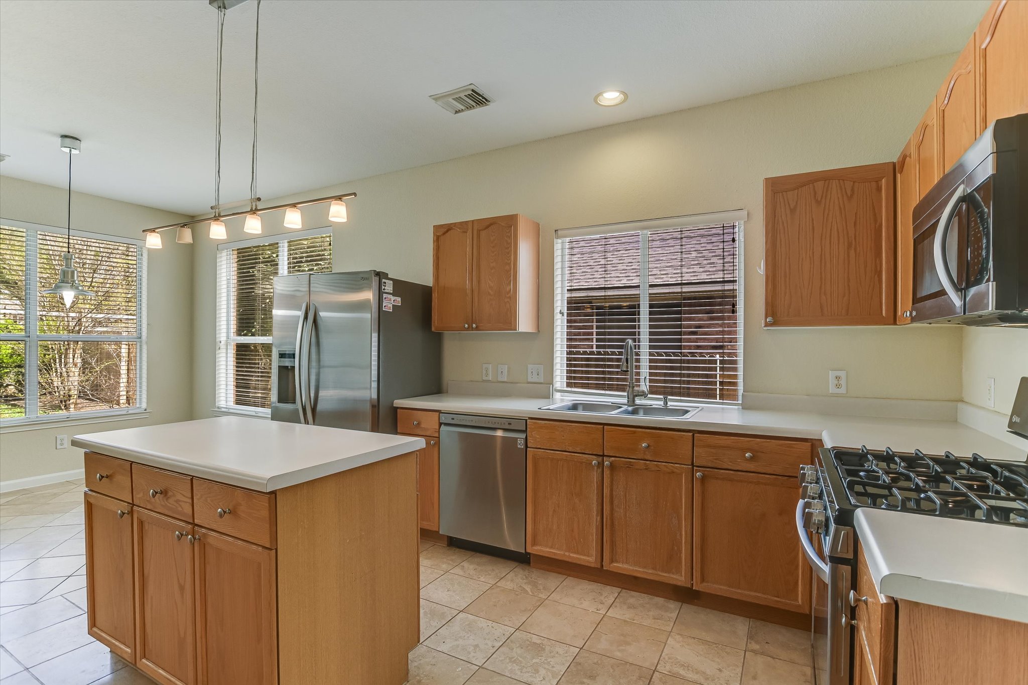 2218 Equestrian Trail Austin, TX 78727 - Photo 14 of 39 Kitchen with stainless steel appliances, light countertops, light tile patterned flooring, wood finish cabinetry, and decorative light fixtures