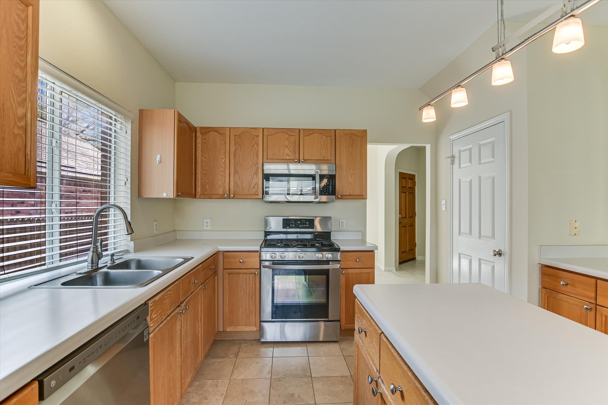 2218 Equestrian Trail Austin, TX 78727 - Photo 15 of 39 Kitchen with stainless steel appliances, light countertops, arched walkways, decorative light fixtures, and light tile patterned flooring
