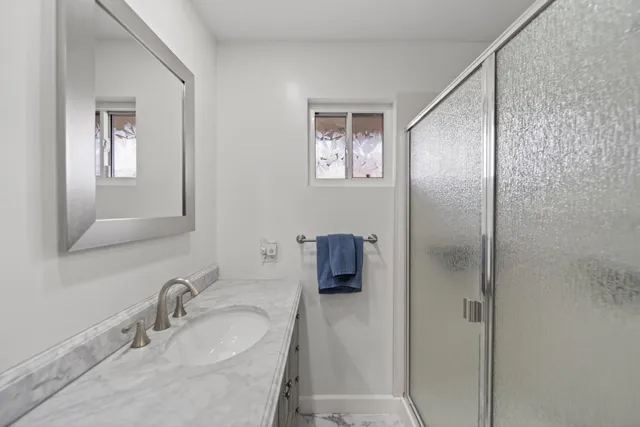 a bathroom with a granite countertop sink a mirror and shower