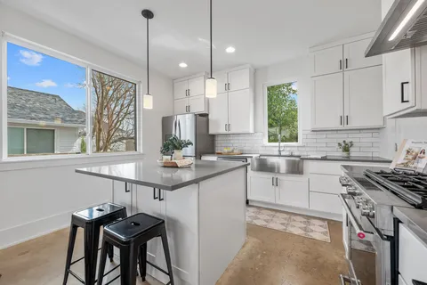 a kitchen with stainless steel appliances granite countertop a sink a stove a refrigerator and chairs