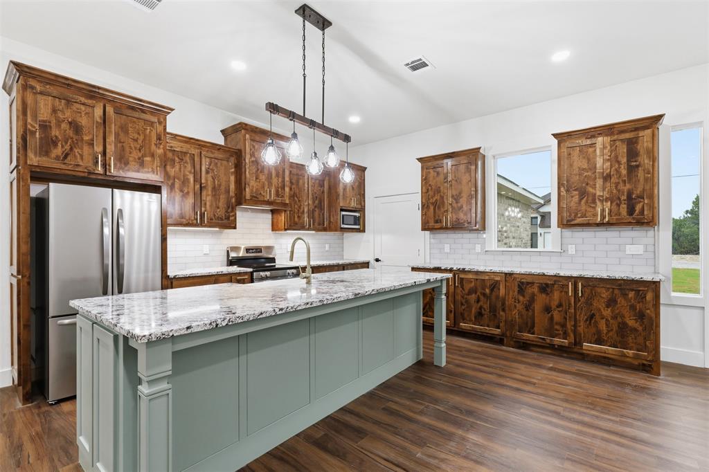 1413 Ridgeview Circle Granbury, TX 76048 - Photo 7 of 35 Spacious kitchen featuring a large island with granite countertop, wood-finish flooring, undermount sink with a gooseneck faucet, white subway tile backsplash, and dark wood cabinetry